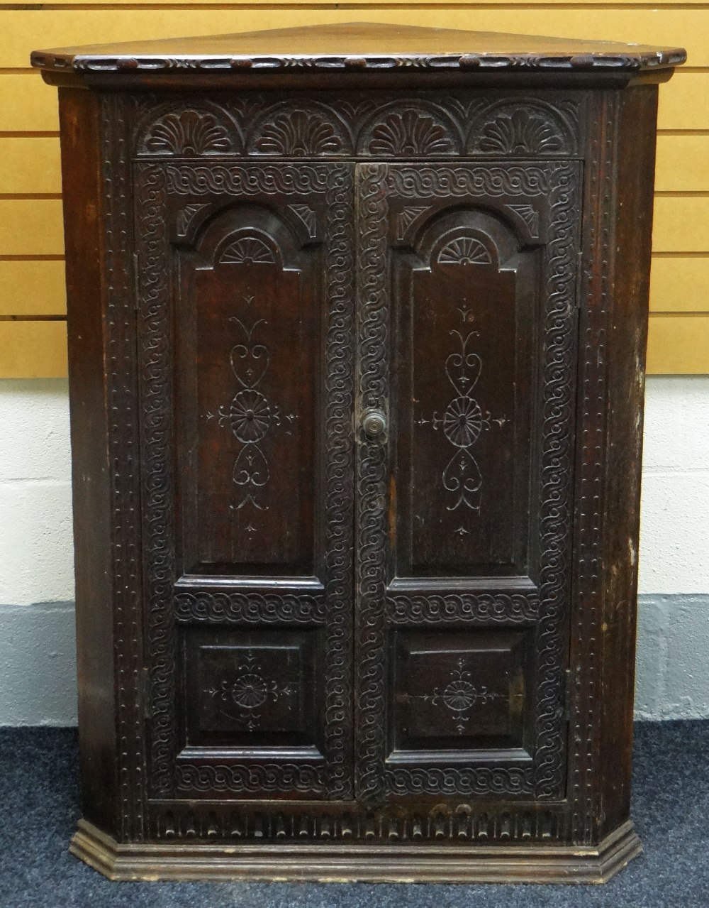 AN EARLY NINETEENTH CENTURY CARVED OAK CORNER CUPBOARD composed of two unglazed doors decorated with