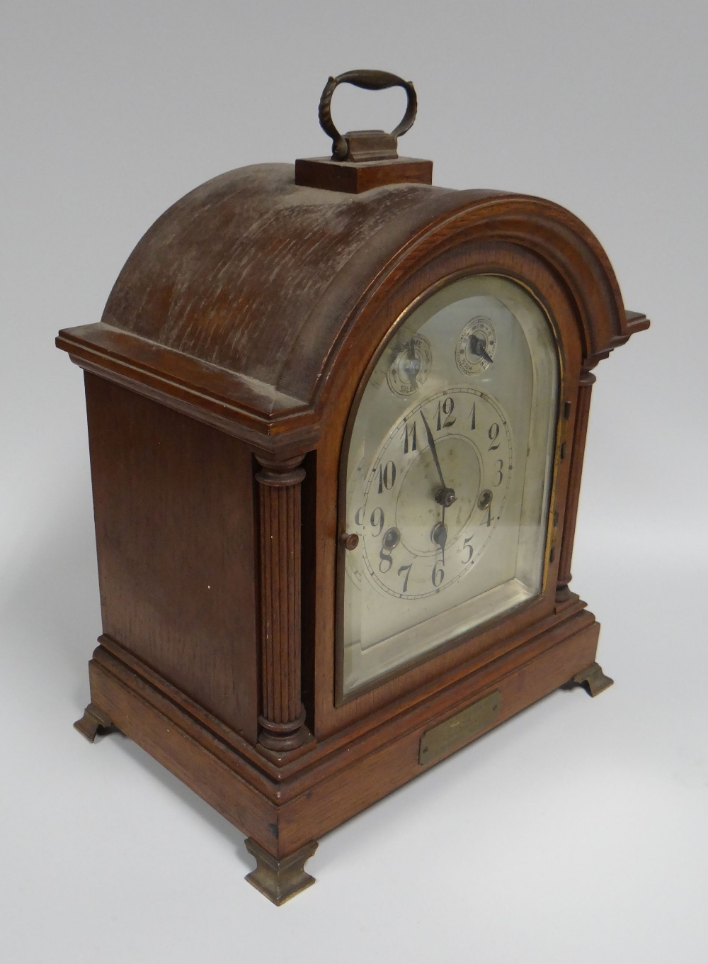 AN OAK ENCASED BRACKET-CLOCK having an arched silver dial with Arabic numberals and two subsidiary