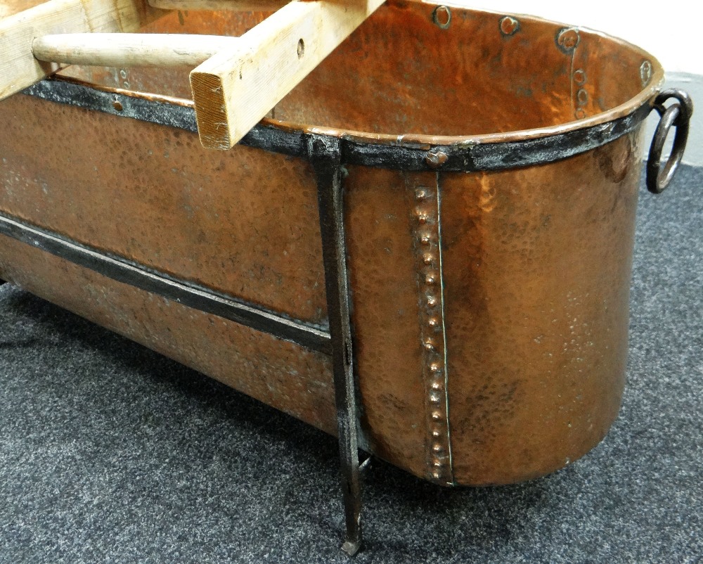AN ANTIQUE BEATEN & RIVETED COPPER BATH raised on a mounted iron frame with ring handles and - Image 2 of 2