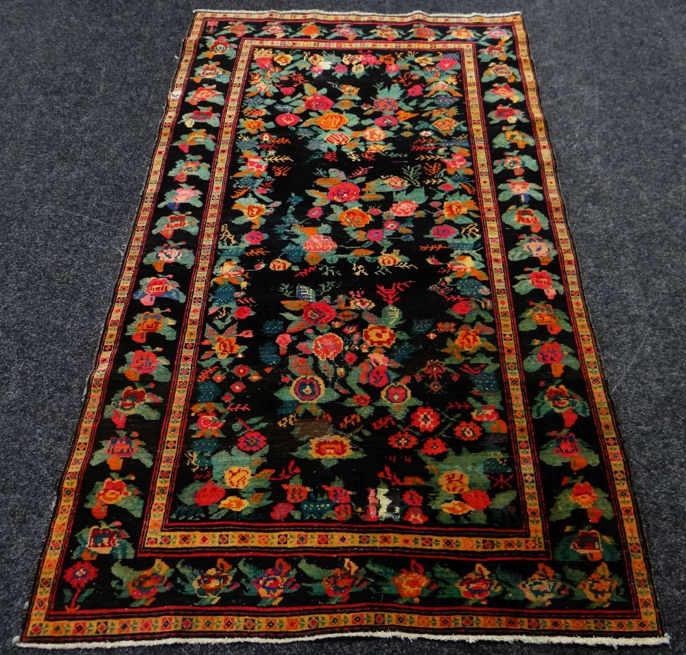 AN ANTIQUE PERSIAN CARPET of black ground with floral decoration, 233 x 130cms