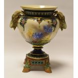 A HADLEY WORCESTER VASE WITH TWIN GOAT-HEAD HANDLES and raised on four hoof feet, painted with