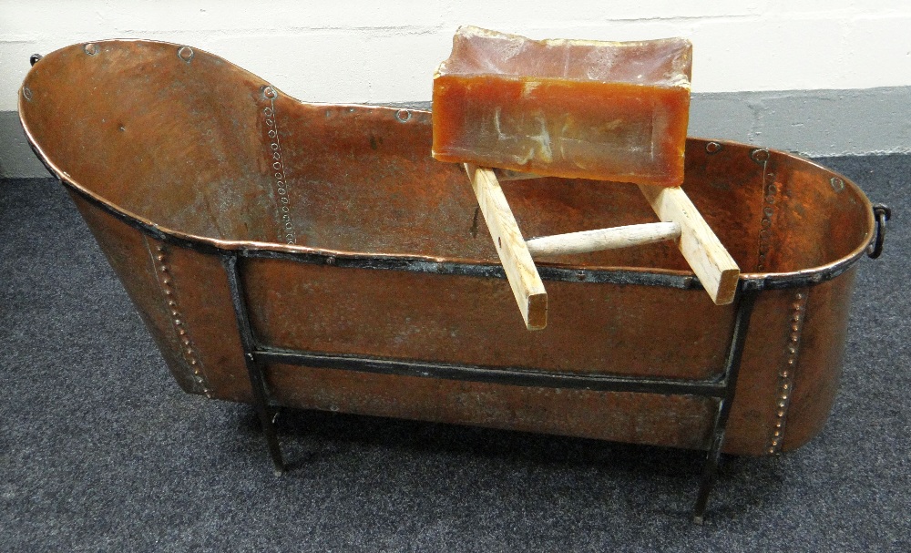 AN ANTIQUE BEATEN & RIVETED COPPER BATH raised on a mounted iron frame with ring handles and