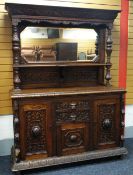 A HEAVILY CARVED OAK MIRROR-BACK SIDEBOARD with an arrangement of drawers and centre cupboard with