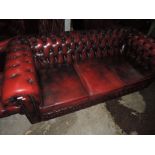 A red leather Chesterfield settee and two similar wing back armchairs and footstool