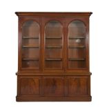 A VICTORIAN MAHOGANY BOOKCASE, the moulded cornice above three arched glazed panel doors enclosing