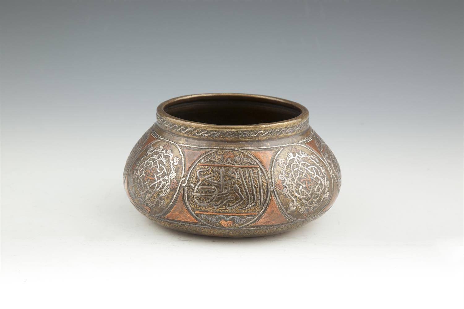 AN ISLAMIC BRASS AND SILVER INLAID BOWL OF SQUAT CIRCULAR FORM, 17cm diameter.