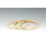 A CHINESE CARVED IVORY BANGLE, c.1900; together with another of slightly smaller dimensions and a