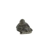AN INUIT CARVING OF AN ESKIMO, modelled in crouched position, pulling a fish tail, signed to base.