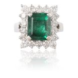 AN EMERALD AND DIAMOND CLUSTER RINGThe rectangular step-cut emerald, weighing 5.35cts, within a