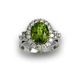 Sortija rosetón de peridoto oval orlado de brillantes en oro blanco de 18K. Peso total aprox btes: