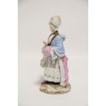 A Meissen porcelain standing female figure wearing lace bonnet & colourful lace-trimmed gown &