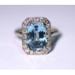 An 18ct white gold ring set emerald-cut aquamarine within a border of small diamonds.