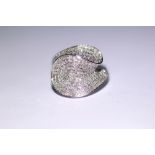 A diamond dress ring of contemporary swirl design, pave-set with numerous small stones, & with