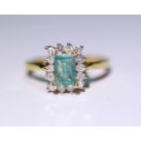 An emerald ring, the large rectangular stone set within a border of fourteen small diamonds, to a