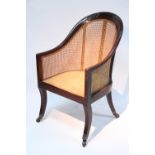 A Regency rosewood bergere with carved rounded back, on reeded sabre legs with brass toes & castors.