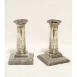 A pair of Edwardian dwarf candlesticks, the round columns embossed with acanthus leaves & bell-