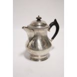 A baluster-shaped hot water jug with hinged domed lid, gadrooned rim, & ebonised scroll handle,