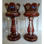 A pair of Edwardian ruby glass lustre vases, each having a crown top, over a baluster shaped column,