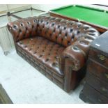 A two person Chesterfield, button upholstered in a brown hide, raised on turned,