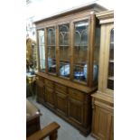 A modern oak display cabinet with a fretworked frieze, over four glazed panelled doors,