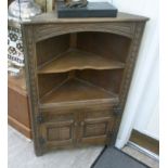A modern Old English style stained oak corner cupboard with an open shelf, over a pair of carved,