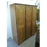 A modern honey coloured pine wardrobe with a moulded cornice, over three panelled doors,