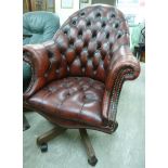 A modern rotating desk chair, button upholstered in a maroon hide,