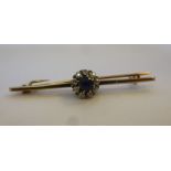 A gold coloured metal bar brooch, claw set with a sapphire,