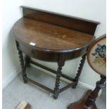 A 1920s stained oak demi-lune hall table with a low upstand and a frieze drawer,
