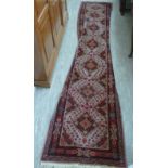 A Turkish runner with repeated diamond shaped motifs on a cream coloured ground 28'' x 137''