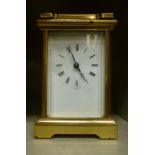 A modern lacquered brass cased carriage timepiece with bevelled glass panels and a folding top