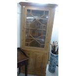 A modern waxed pine corner unit, the upper section with a glazed door, enclosing three shelves,