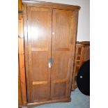 A stained wood wardrobe, the panel doors enclosing interior shelf, raised on a plinth base.