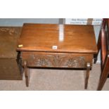 A stained oak sewing box, the hinged top above carved panel, raised on shaped legs.
