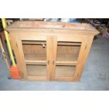 A stripped pine cupboard, the flared cornice above glazed panel doors enclosing shelves.