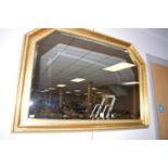 A shaped bevelled wall mirror, in gold painted frame decorated with leaf and bead design.