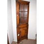 A mid 20th Century oak corner cabinet, the dentil cornice above glazed panel door enclosing shelves,