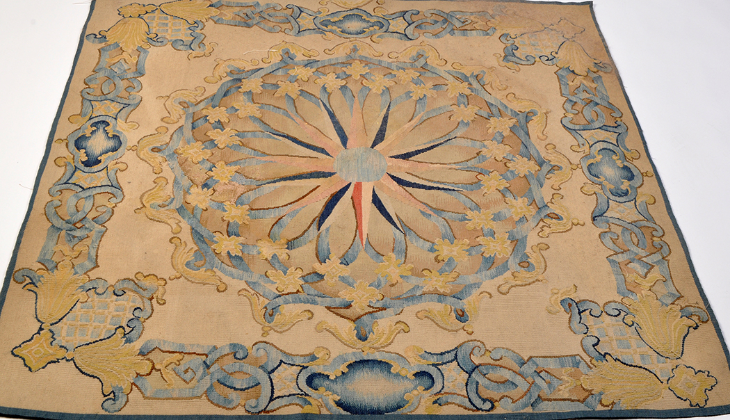 An Aubusson type rug, with central rosette and leaf scrolls in blues and golds on fawn ground,