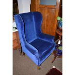 A wing back easy armchair raised on square legs with brass castors, later covered in blue dralon.