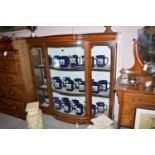 A bowfront inlaid stained wood display cabinet with glazed panels and underlying drawer.