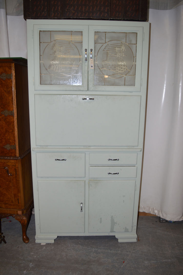 A green painted larder cabinet, with etched glass panels above a fall-flap with enamel surface,