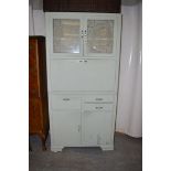 A green painted larder cabinet, with etched glass panels above a fall-flap with enamel surface,