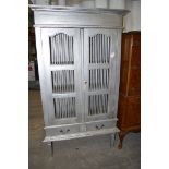 A silver painted larder cabinet, the spindle panel doors enclosing shelves, two drawers under.