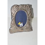 A silver mounted photograph frame of shaped form, decorated with leaf scrolls.