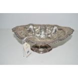 A white metal oval dish, embossed and pierced with floral decoration, standing on flared foot.