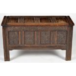 A late 17th Century style oak coffer, the solid panel top above carved front decorated with scrolls,