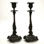 A pair of bronze patinated candlesticks with cast foliate designs in the rococo manner,