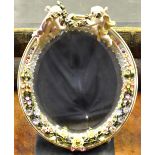 A Sitzendorf porcelain oval easel mirror with floral encrusted frame surmounted by cherubs with