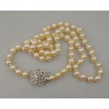 A single row uniform cultured pearl necklace on white metal diamond set cluster three-strain snap