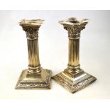 An Edwardian pair of classical column loaded silver candlesticks on moulded square bases, John